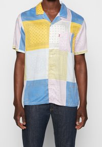 Korte mouwen overhemd met knopen, voorzien van een patchwork ontwerp in geel, blauw en lila met paisley patronen. Inclusief een borstzak aan de linkerkant.