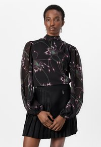 Blusa nera con motivo floreale in rosa e verde, con maniche a palloncino e colletto alto. Abbinata a una gonna nera plissettata.