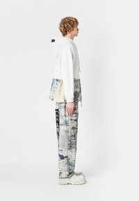 Sudadera con capucha de parte superior blanca y sección inferior de un patrón azul-gris, combinada con pantalones a juego con el mismo patrón y calzado grueso blanco.