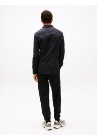 Camisa negra de manga larga con cuello abotonado, combinada con pantalones jogger negros. Zapatillas grises con detalles de malla y textil.