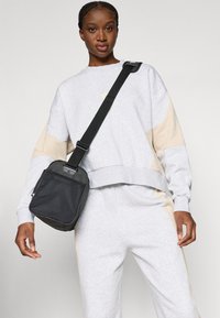 Γκρι φούτερ με μπεζ λεπτομέρειες, συνδυασμένο με αντίστοιχες γκρι φόρμες. Μία μικρή μαύρη τσάντα χιαστί διαθέτει εμπρόσθιο πάνελ από διχτυωτό υλικό και ρυθμιζόμενο λουρί.