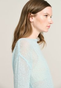 Light blue, loose-knit sweater with a high neckline and dropped shoulders. Soft texture with a slightly sheer appearance.