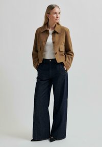 Barna báránybőr dzseki, két elülső zsebbel, amelyet magas derekú sötétkék farmer, bő szárú nadrággal párosítanak. A megjelenést sima fekete, hegyes orrú cipők teszik teljessé.