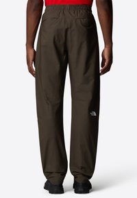 Pantalons en nylon marron avec une taille élastique, arborant un logo blanc sur la jambe gauche, et une coupe décontractée qui se resserre en bas.