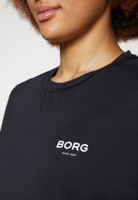 Svart T-skjorte med korte ermer og rund hals. Har en hvit "BORG"-logo med "SINCE 1956" under på venstre bryst.