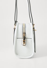 Sac en cuir blanc avec une forme compacte, fermeture éclair en or et sangle noire en accent. Présente des coutures nettes et un design minimaliste épuré.