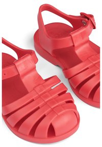 Raudoni plastikiniai šlepetės su uždaru pirštu, horizontaliais diržais ir reguliuojama sagtimi. Tekstūruota pado dalis ir atviras galas vėdinimui.