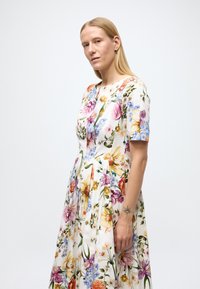 Bloemenjurk met een witte basis en kleurrijke patronen van rozen en madeliefjes, korte mouwen, ronde halslijn en geplooide rok.