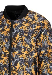 Bomberjack in zwart stof met een draaiend patroon in oranje, grijs en wit, een ritssluiting aan de voorkant en een geribde kraag.