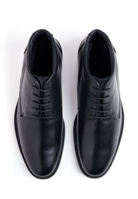 Chaussures en cuir noir avec texture lisse, design classique et six œillets. Équipées d'un bout arrondi et d'un détail de piqûre minimal sur le côté.