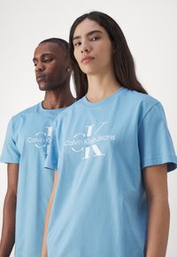 Gaiši zilas kokvilnas t-krekli, kas rotāti ar baltu "Calvin Klein Jeans" logo, ar apaļu kakla izgriezumu un īsām piedurknēm.
