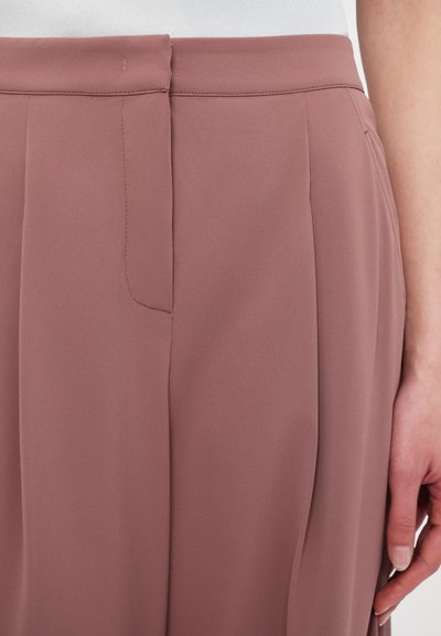 Pantaloni rosa antico caratterizzati da una texture liscia e setosa, con pieghe frontali e una tasca laterale nascosta, progettati per un fit aderente.