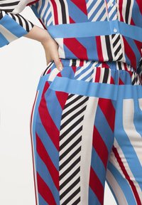 Completo colorato e fantasioso caratterizzato da forme geometriche in rosso, blu, nero e bianco. Tessuto morbido con vita elastica e bottoni.