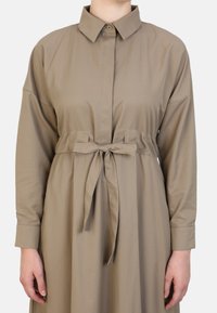 Khaki shirtjurk van soepel materiaal, met een knoopsluiting bij de kraag, lange mouwen en een tailleriem voor een gedefinieerde silhouet.