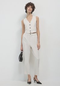 Completo beige chiaro a due pezzi composto da un top aderente senza maniche con bottoni, pantaloni su misura coordinati e tacchi a punta neri.
