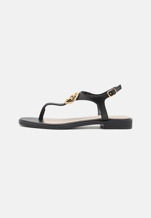Zwarte leren teenslipper met een gouden cirkelaccent, vlakke zool en een verstelbare gespband bij de enkel voor een veilige pasvorm.