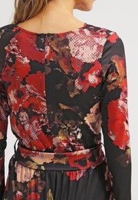 Abito a fantasia floreale caratterizzato da un vivace design rosso e nero, maniche lunghe, tessuto morbido e dettaglio in vita arricciato.
