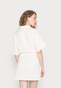 Vestido de algodão branco, de mangas curtas, com corte solto, cintura ajustada e superfície ligeiramente texturizada. Design minimalista, com detalhe na gola.