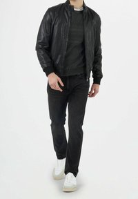 Giubbotto bomber in pelle nera sopra un maglione grigio a righe, abbinato a jeans scuri e sneaker bianche con dettagli grigi.