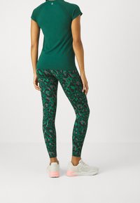 Grön sportig topp kombinerad med högmidjade leggings med ett rosa och mörkgrönt leopardmönster. Modellen bär ljusgrå sneakers.