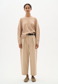Beżowy, oversize sweter dzianinowy z długimi rękawami, połączony z beżowymi spodniami o wysokim stanie i szarymi butami wsuwanymi. Czarny pasek podkreśla stylizację.