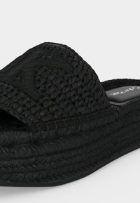 Sandale slide noire tissée avec semelle épaisse tressée et large bride avec un détail de motif en losange.