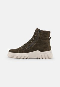 High-top sneakers in dark green suede with a textured surface, prominent side zipper, and a chunky cream-colored sole with ridges.