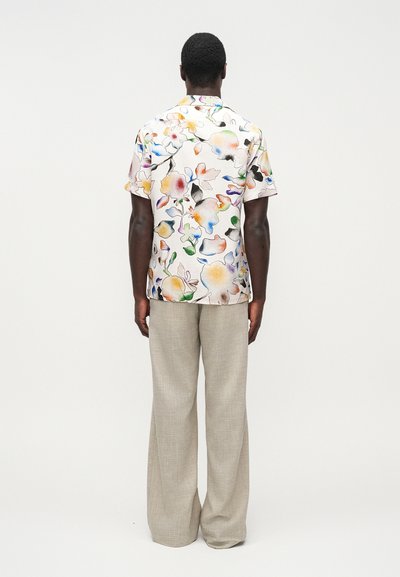 Κοντομάνικο, πολύχρωμο πουκάμισο με λουλούδια σε ανοιχτό ροζ φόντο, σε συνδυασμό με ανοιχτό γκρι παντελόνι με φαρδιά μπατζάκια, προβολή από πίσω.