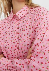 Pink blouse with a cherry pattern, featuring a collar, long sleeves, and button-down front. Lightweight fabric with a smooth texture.