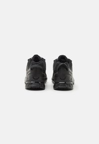 Chaussures de sport noires avec une tige en maille texturée, un talon de soutien et une semelle en caoutchouc à motifs, dotées d'accents réfléchissants.
