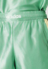 Žalios sportinės šortai, pagaminti iš lygaus, lengvo audinio, su elastingu diržu, ant kurio yra baltas "adidas" logotipas. Su šoninėmis kišenėmis.