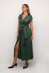 Green wrap dress in a satin material, featuring a deep V-neck, short sleeves, a waist tie, and a side slit. Worn with black heels.