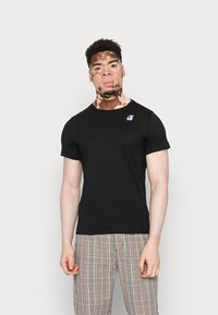 T-shirt nera aderente a maniche corte, con un piccolo logo sul lato sinistro. Abbinata a pantaloni a quadretti in diversi colori.