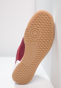 Bordové tenisky s texturovaným svrškem a bílým gumovým špičkou. Hnědá gumová podrážka má vzorovaný dezén pro lepší přilnavost. Vybavení s embosovaným logem Reebok.