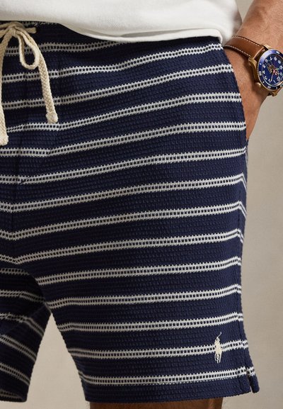 Marineblå og hvitstripede teksturerte shorts med snøring i livet, båret med en brun klokkerem i lær på venstre håndledd.