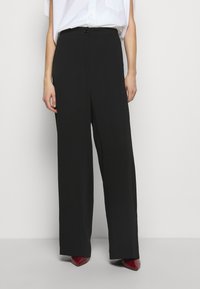 Svarta byxor med breda ben och en mjuk textur, hög midja och en enkel knappstängning. Bärs tillsammans med en ljus skjorta och röda klackar.