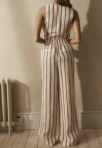 Combinaison en lin rayée avec ceinture élastique, présentant des jambes larges, deux poches arrière et des rayures verticales noires sur un fond clair.