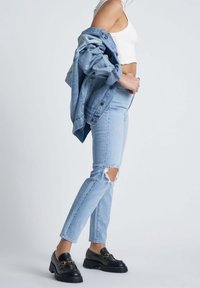 Light blue denim jeans with ripped knees, paired with a matching denim jacket. Black loafers with chunky soles and golden accents.