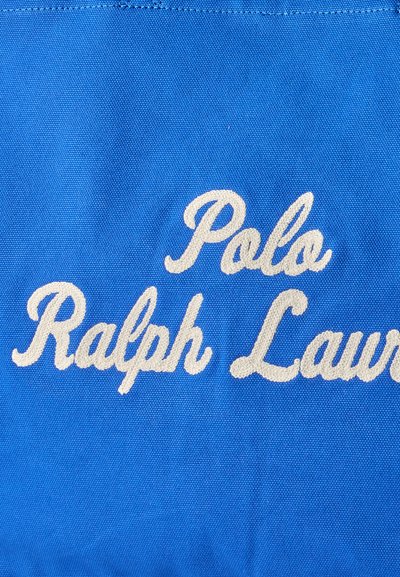 Μπλε ύφασμα με λευκό κεντητό κείμενο που απεικονίζει τη φράση «Polo Ralph Lauren» με γραφή σε καλλιγραφικό στυλ.
