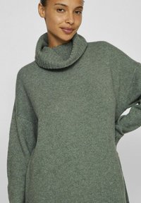 Överdimensionerad grön stickad tröja med hög ribbad krage, avslappnad passform och långa ärmar, med en mjuk textur och minimalistisk design.