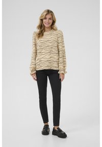 Ljusbeige tröja med svart vågmönster, långa ärmar med rynkade manschetter, ihop parat med svarta slim-fit jeans och svarta loafers.