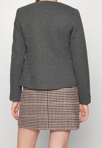 Grijze herringbone structuur blazer met lange mouwen, gecombineerd met een roze en bruine hertenprint rok. Schone lijnen en een getailleerde pasvorm.
