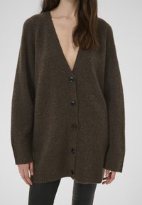 Barna gyapjú kardigán mély V-nyakkivágással, bordázott mandzsettákkal és hat fekete gombbal az elején. Texturált anyag és laza szabás.