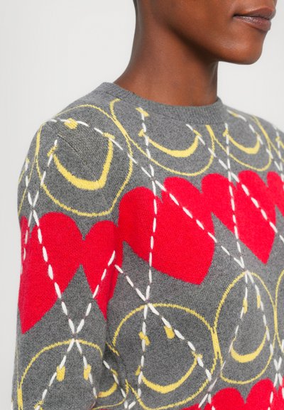 Pulover gri cu inimi roșii și modele circulare galbene. Are cusături albe și un gât rotund. Textură moale, design casual.
