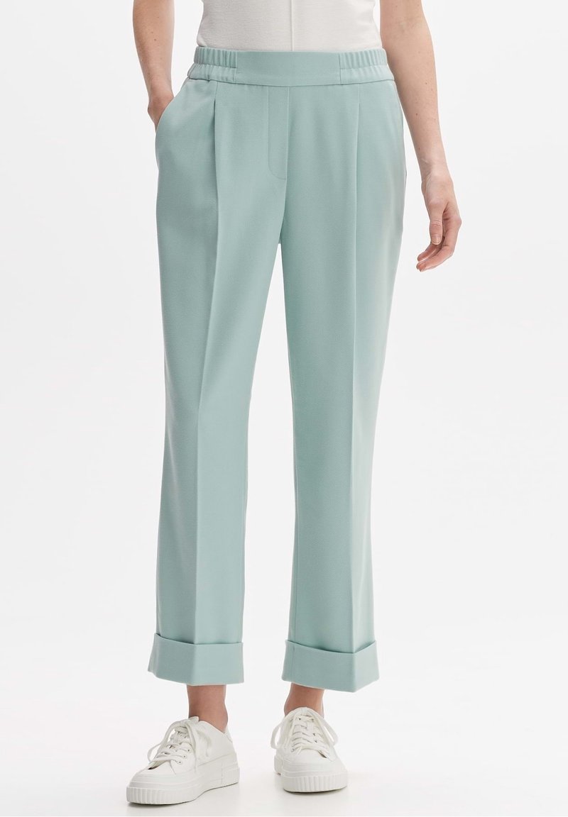 Pantalon bleu clair à revers avec taille élastique, porté avec des baskets blanches et un haut blanc rentré, montrant les poches avant et latérales.