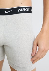 Sivé bavlnené boxerky s čiernym pásom s logom Nike. Materiál má jemnú textúru a priliehavý strih, s viditeľnými švami a lemami.