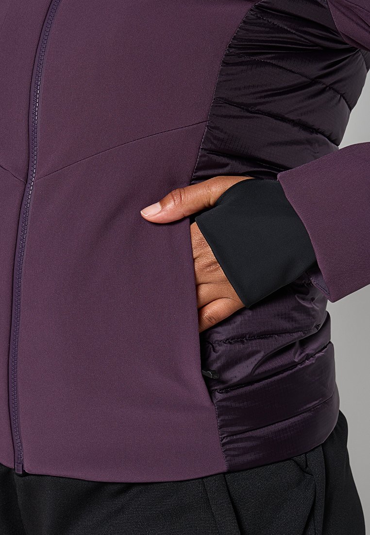 Giacca viola con una combinazione di texture lisce e trapuntate, con chiusura a zip e accenti neri sui polsini. Include una tasca laterale.