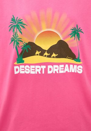 T-shirt en coton rose avec un design graphique représentant un soleil, des montagnes, des chameaux et des palmiers. Texte "DESERT DREAMS" en police blanche en gras.