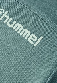 Lyseblå sweatshirt med struktureret stof og ordet "Hummel" i hvidt på tværs af brystet, der fremhæver et enkelt, moderne design.
