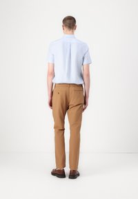 Lyseblå kortermet skjorte med en bakfelle, kombinert med brune smale bukser med elastisk liv og sidelommer.